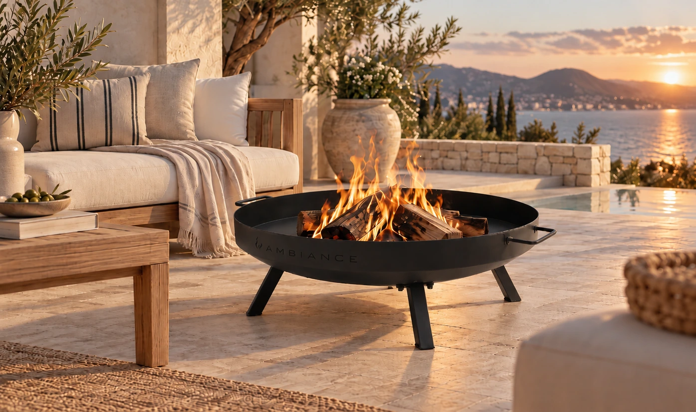 Black metal fire pit with burning logs beside outdoor seating on a sunset terrace